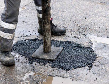 worker pushing bitumen asphalt in the hole. road repair and maintenance